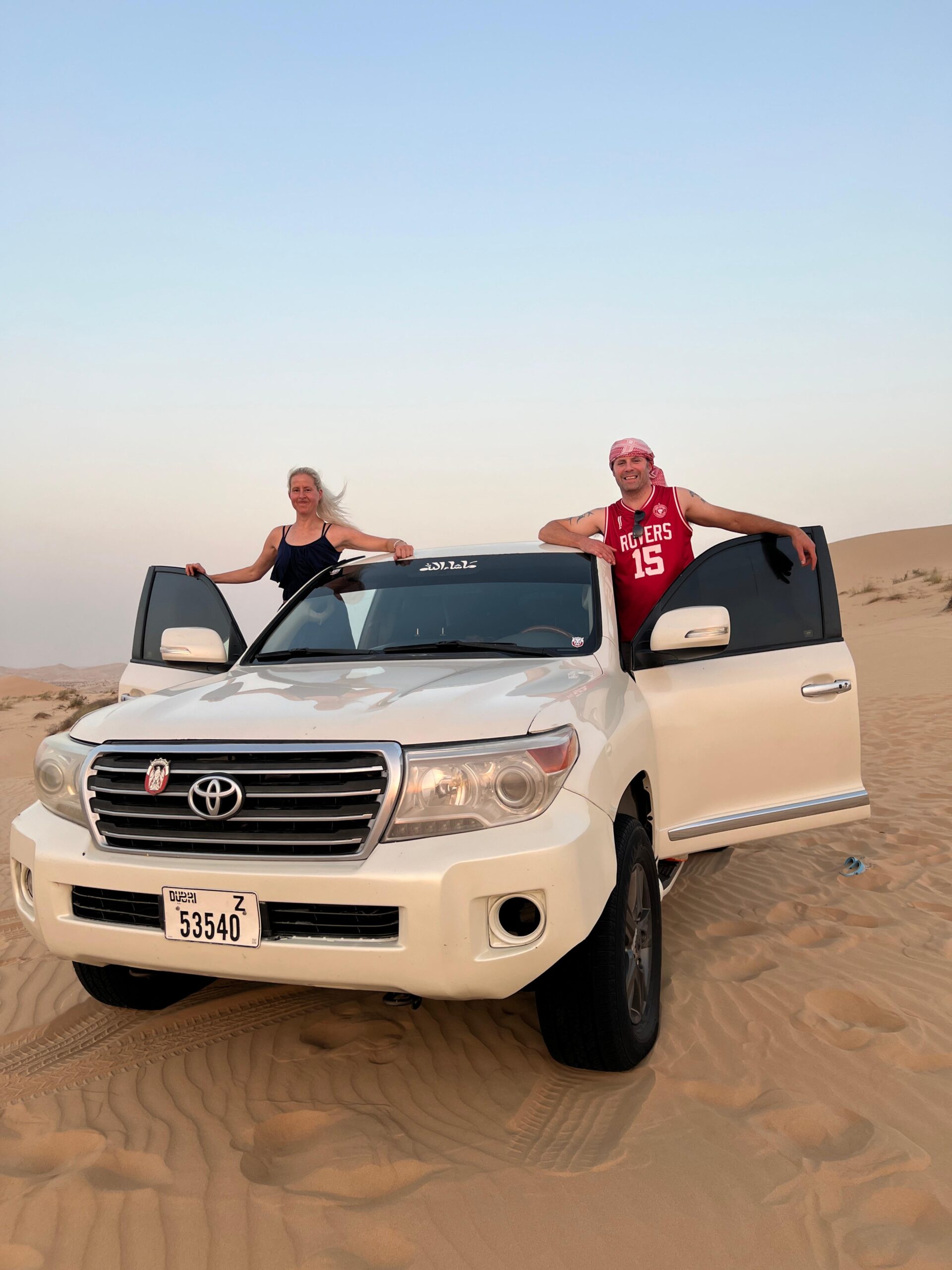 A family laughing and having fun while trying desert sandboarding on the golden sands